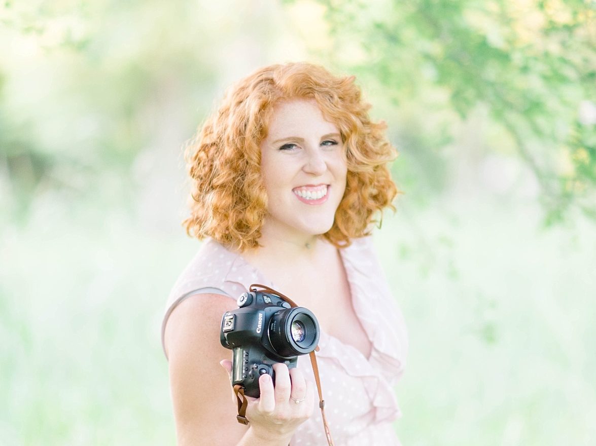 New Orleans wedding photographer Elizabeth Collins in a pink dress with short curly hair holding her camera